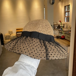 Detail of hand-woven straw hat featuring black polka dot mesh veil and ribbon bow