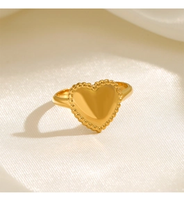 Macro view of golden heart-shaped ring with beaded edges on a white satin background