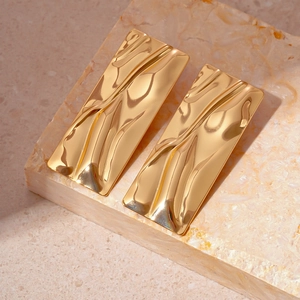 Detail of golden rectangular metal earrings with liquid wave texture on a stone base