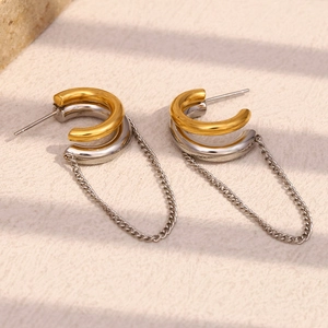 Macro detail of two-tone C-shaped hoop earrings with dangling gold and silver chains