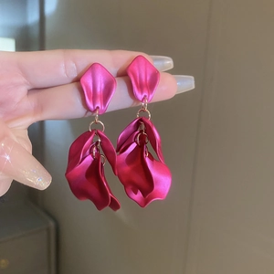 Close-up of vibrant rose red layered petal earrings with golden rings on hands