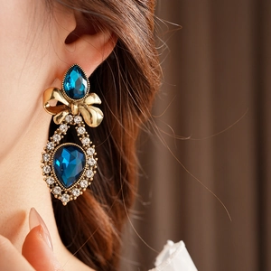 Detailed view of vintage gold bow earrings with teardrop blue stones and crystals
