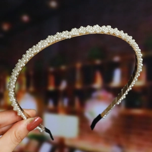 Detailed view of woven pearl headband with white beads on a golden metal frame