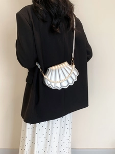 Silver shell-shaped crossbody bag with pearl chain detail shown on a model