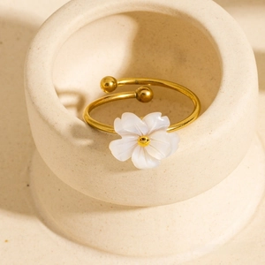 Detailed view of an open 18K gold-plated flower ring with white shell petals on a ceramic dish