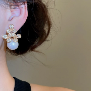 Close-up of elegant gold flower stud earrings with zircon and large round pearl on ear