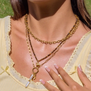 Detail of layered gold titanium necklace with brown beads, white pearl, and cross pendant