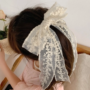 Elegant oversized white lace bow hair clip with floral embroidery on wavy brown hair