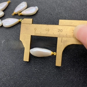 Macro view measuring a 17mm irregular Baroque freshwater pearl with gold bail using calipers