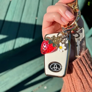 Handheld view of a white silicone car key case with strawberry and daisy charms