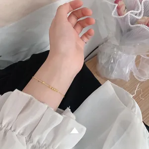 Detailed view of a minimalist gold beaded chain bracelet worn on a female wrist