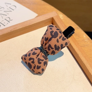 Close-up of leopard print fabric bow hair clip on a wooden tray with aesthetic background