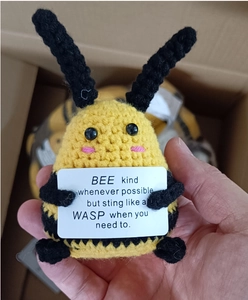 Close-up of handmade crochet bee plush toy holding a motivational sign with text