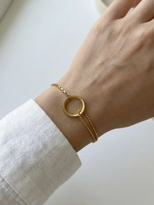 Detail of 18k gold double-layered bracelet with ring and bead chain on woman's wrist