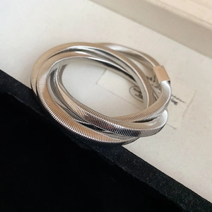 Close-up of triple-layered silver spiral snake chain bracelet on textured backdrop