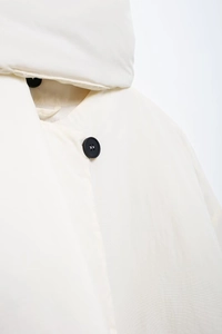 Detailaufnahme einer minimalistischen cremefarbenen Steppjacke mit schwarzem Knopfdetail