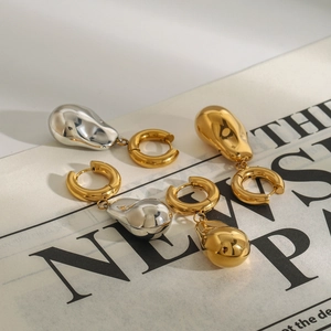 Vue détaillée de boucles d'oreilles gouttes en métal poli or et argent sur un journal