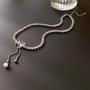 Detail of silver bow necklace featuring sparkling zircons and elegant pearl tassels