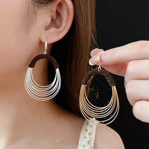 Close-up of layered metal oval earrings with gold and silver finish and brown cord details