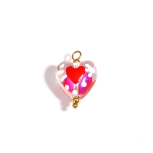 Detail showing a pink heart glass pendant with red inner core and gold metal fittings