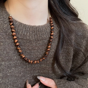 Close-up of tiger eye beaded necklace worn over a brown sweater for a vintage aesthetic