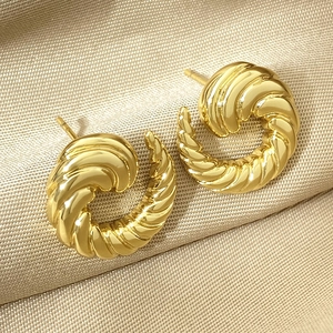 Macro detail of golden twisted spiral stud earrings on elegant silk background