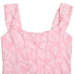 Dettaglio del corsetto rosa con tessuto testurizzato e spalline larghe su sfondo bianco
