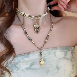 Detail view of ethnic layered necklace featuring green beads and metal leaf pendant charms