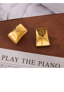Close-up of gold rectangular stud earrings on a leather surface and magazine