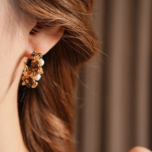 Macro detail of C-shaped gold earrings with brown tiger eye stones and white pearls