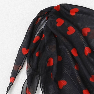 Détail du tissu en maille noire avec motifs cœurs rouges et finition de couture roulée