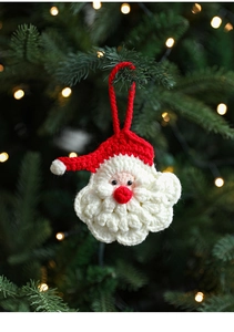 Close-up of handmade knitted Santa Claus ornament hanging on a green Christmas tree branch