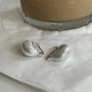 Macro shot of silver drop earrings with brushed metal texture on soft white fabric