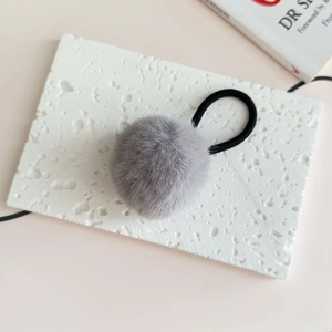 Close-up of a soft grey faux fur pompom hair tie on a minimalist textured stone surface