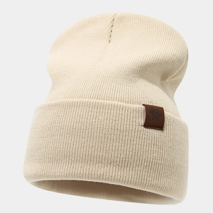 Close-up of cream ribbed knit beanie featuring a brown leather snowflake patch detail