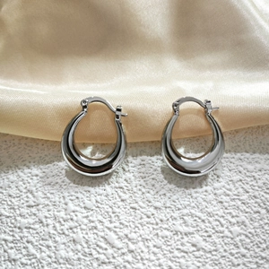 Detail view of silver crescent hoop earrings resting on white texture and gold silk fabric