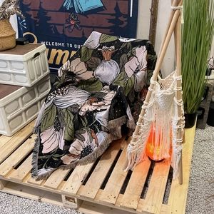 Bohemian floral camping blanket with tassels displayed on a wooden tray in outdoor setting
