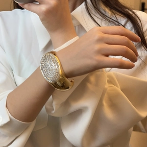 Detail eines breiten goldenen ovalen Armreifs mit funkelnden Steinen an einem Model