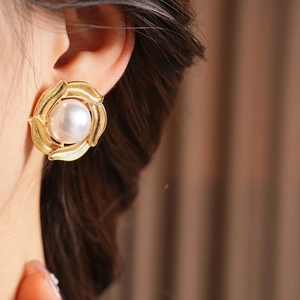 Close-up of pearl earring on model with matte gold floral texture and soft focus