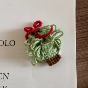 Close-up of handmade crochet Christmas tree hair clip with a red bow on wood surface