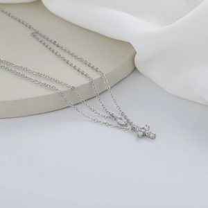 Macro detail of silver layered necklace with zircon cross and marquise stone on silk