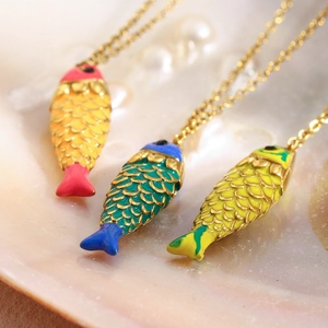 Macro shot of 18K gold fish pendants with colorful enamel details on shell background