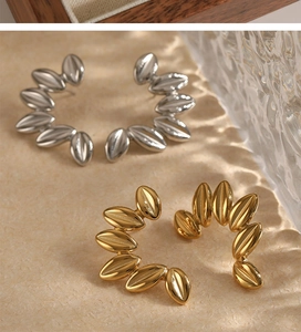 Detail view of gold and silver stainless steel leaf-link C-shaped earrings on textured base