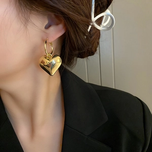 Nahaufnahme von großen goldenen Herz-Ohrringen mit poliertem Metall-Finish am Model