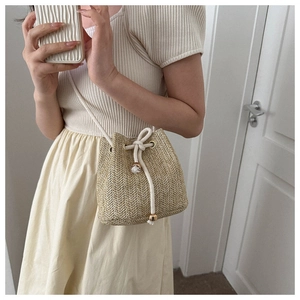 Detail of hand-woven straw bucket bag with cotton drawstring closure and gold hardware