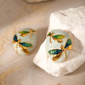 Close-up of oval stainless steel earrings featuring gold dragonflies on light blue enamel