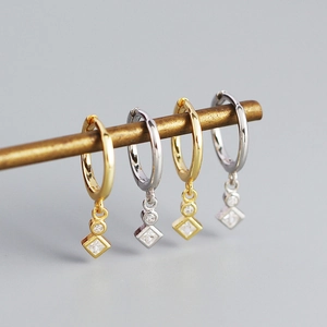 Macro view of gold and silver S925 square crystal hoop earrings on a metal display
