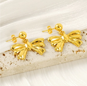 Detailed view of elegant gold bow earrings on a textured stone surface and silk fabric