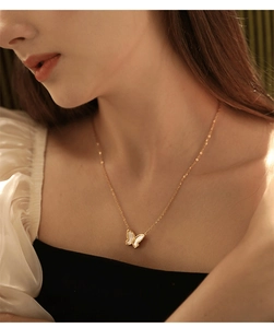 Close-up of elegant gold butterfly necklace with white shell inlay worn by a model