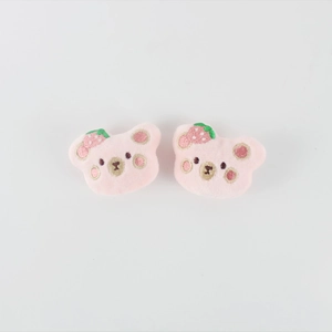 Detail view of two plush pink bear pins featuring strawberry embroidery and soft texture
